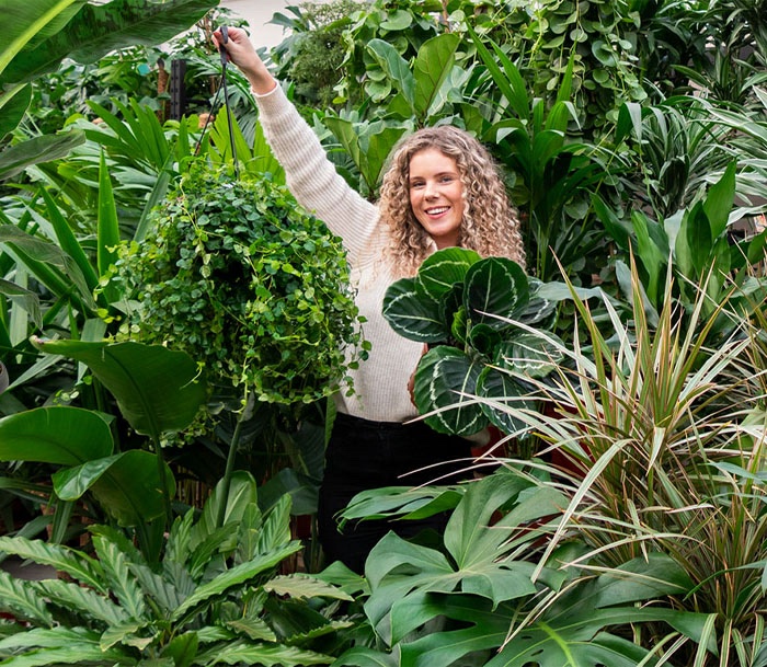 vrouw staat tussen planten en houd er een aantal vast